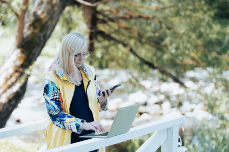busy business woman with laptop and mobile phone communicating remotely in city parkの写真素材