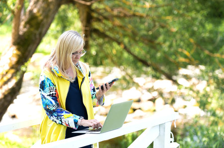 busy business woman with laptop and mobile phone communicating remotely in city parkの写真素材