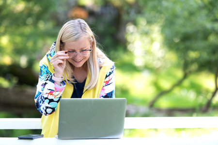 Smiling business woman standing in city park and looking at laptop screenの写真素材