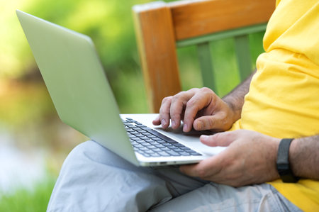 A man working and typing on laptop keyboard while sitting in the parkの写真素材