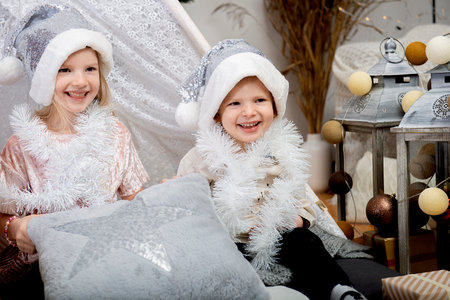 Two happy kids - girl and boy wearing a Christmas hats  sitting among the holiday decorations at homeの写真素材