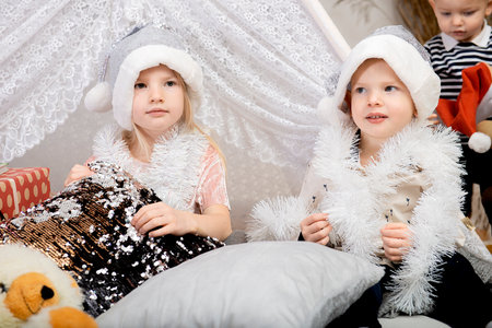 Two kids- boy and girl wearing a Christmas hat sitting among the holiday decorations at homeの写真素材