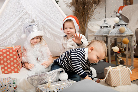 Three cute children kids wearing Christmas hats playing between gift boxes in a decorated house.Merry Christmas and Happy Holidays!の写真素材