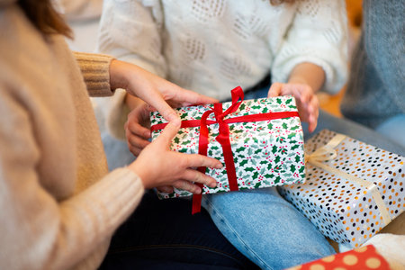 Close up of young women hands wrapping gifts near the Christmas tree at home.の写真素材