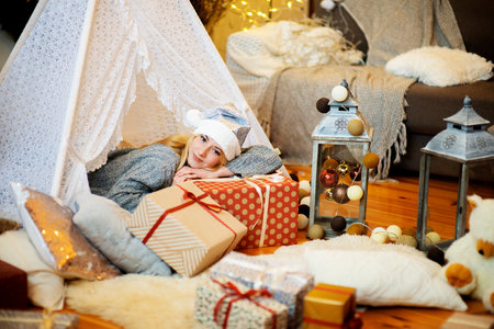 Pretty lady woman laying on Christmas giftboxes wear knitted pullover and santa hat in decorated for festive home living roomの写真素材