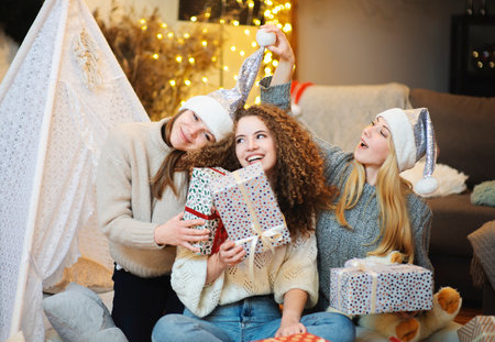 Three happy attractive young women sisters sitting on the floor at home gift wrapping giving Christmas presentの写真素材