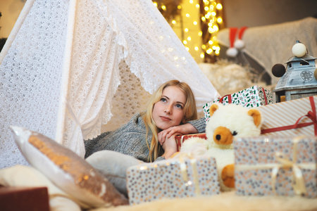 Pretty lady woman laying on Christmas giftboxes wear knitted pullover and santa hat in living roomの写真素材