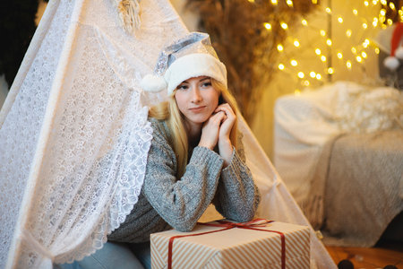 Portrait of beautiful blonde woman with santa hat and Christmas present on bokeh lights backgroundの写真素材