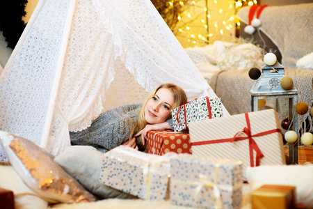 Pretty blonde lady woman girl laying on Christmas giftboxes wear knitted pullover in decorated living roomの写真素材