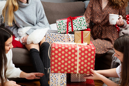 young girls having fun wrapping gifts at home, teamwork of friends packing presents for christmasの写真素材