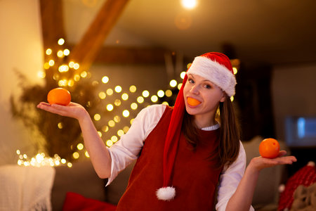 Young attractive woman wear santa hat holding citrus orange fruit mouth having fun in Christmasの写真素材