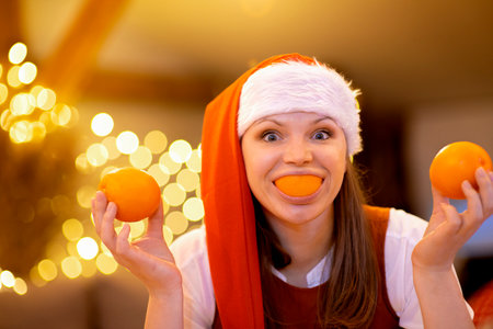 Young attractive woman wear santa hat holding citrus orange fruit mouth having fun in Christmasの写真素材