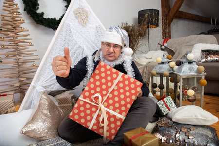 Family grandfather mature man wearing silver santa claus hat holding christmas gift boxes and show thumb upの写真素材