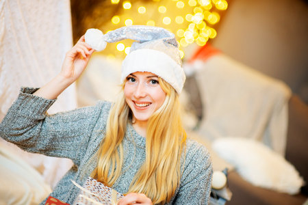 Beautiful blonde woman with santa hat and Christmas present on bokeh lights backgroundの写真素材