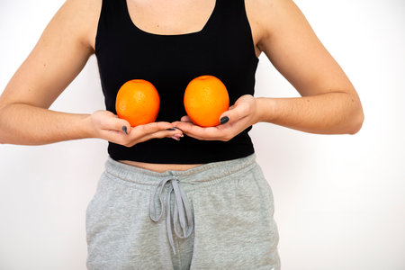 Woman holding two oranges in front of her breast, breast cancer awareness concept