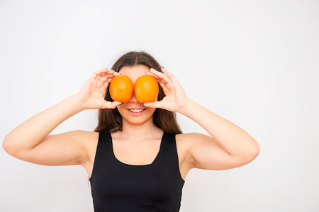beautiful young woman brunette holds oranges in front of her eyes, healthy breakfast or diet conceptの写真素材