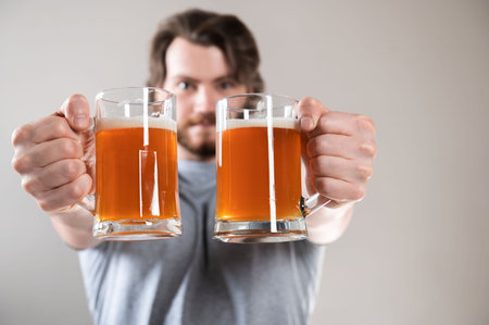 close-up of a young man's hand with two mugs of beer isolated on light gray backgroundの写真素材