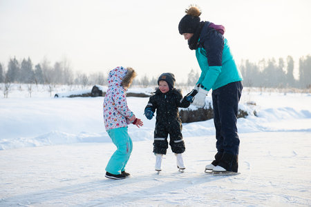 Young mother teaching her little baby boy son ice skating at outdoor skating rink.の写真素材