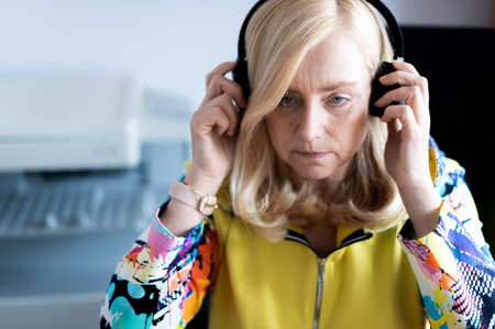 Close-up portrait of focused middle-aged woman wearing headphones watching webinar at office computerの写真素材