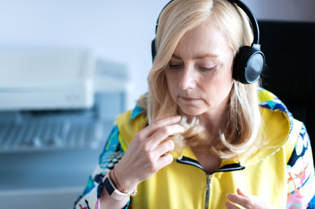 Close-up portrait of focused middle-aged woman wearing headphones watching webinar at office...