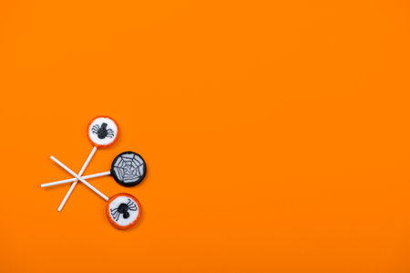 Halloween candy with black spiders and cobweb on orange color background,top view