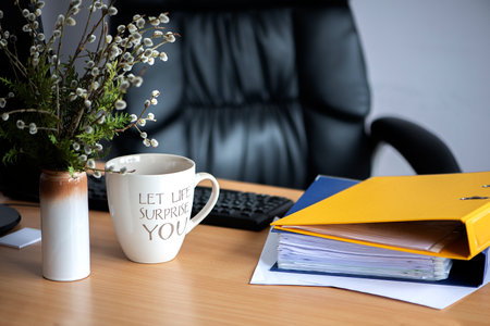 cup of hot coffee mug tea on the working desk with sign "let life surprise you", computer and folder of documentsの写真素材