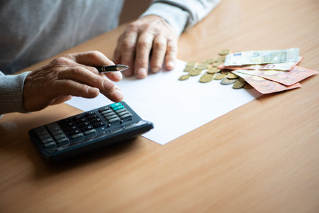 Hands of old senior man with calculator and bills counting euro money at home.の写真素材