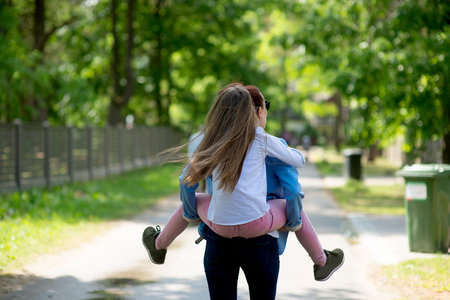 Rear view on young daughter on a piggy back ride with her mother.Happy family having fun outdoorの写真素材