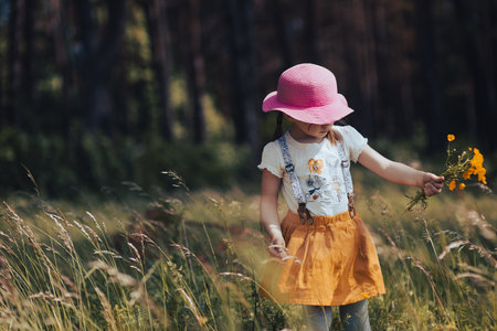 Little stylish girl in a pink hat walks in a flowering summer meadowの写真素材
