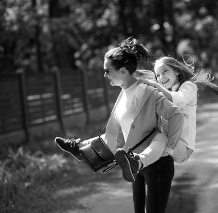 Mother and her daughter playing together at park. Mom carrying on shoulders or back.の写真素材