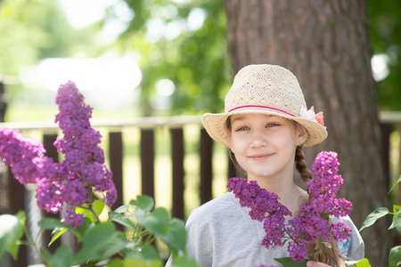 portrait of a beautiful teenage girl with a summer hat and a blossoming lilac branchの写真素材