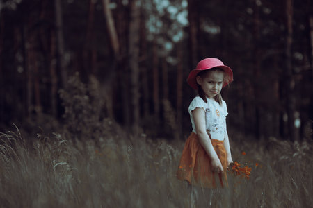 Little angry girl in a pink hat walks in a flowering summer meadowの写真素材