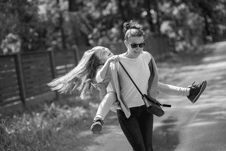 Mother and her daughter playing together at park. Mom carrying on shoulders or back.の写真素材