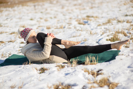 Young attractive woman practicing yoga onsnowy field.Outdoor  activity. Practice yoga asana. Healthy...