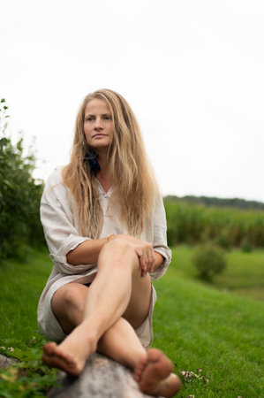 Portrait of young natural woman sitting on wooden log outdoorsの写真素材