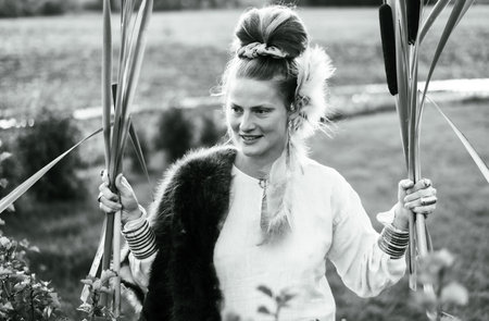Strong young woman with a bulrush grass reed on rural field, portrait monochrome