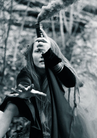 Shaman female holding hand smoke bomb on  tree trunk , black and white portrait