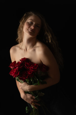 Beautiful woman with bare shoulders and red roses on a dark studio background. Beauty studio portrait. Sensual model with red roses flowers, isolated on black. Charming mature natural female without makeup.の写真素材