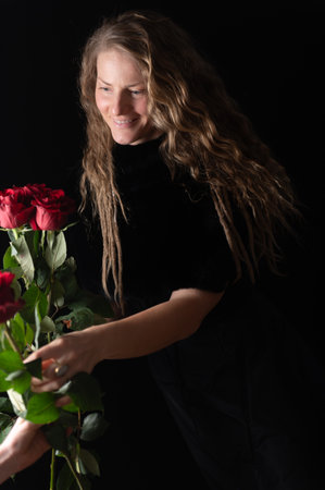 Charming mature natural female without makeup. Pretty woman with red roses on black. Beauty studio portrait. Beautiful model with red roses flowersの写真素材
