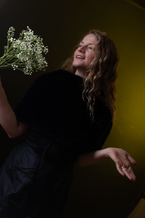 Studio shot of smiling young natural woman with long curly hair holding and smelling white flowers on a dark background, copy space.の写真素材