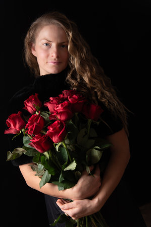 Charming mature natural female without makeup. Pretty woman with red roses on black. Beauty studio portrait. Beautiful model with red roses flowersの写真素材