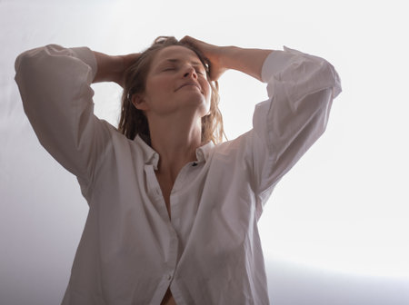 Beautiful woman on a white studio background. Young woman looking up, holding her hands behind her head.の写真素材
