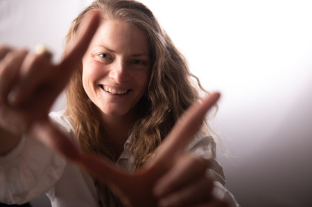 Smiling woman's face framed by fingers on white studio background. Adult female with cheerful face expression.の写真素材
