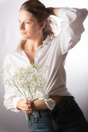 Beautiful young woman holding flowers on white background, white shirt, long curly hairの写真素材