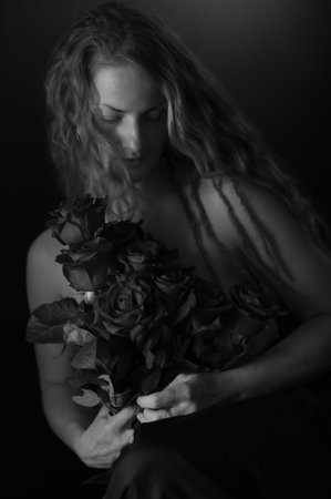 Beautiful woman with bare shoulders and roses on a dark studio background. Beauty monochrome portrait. Sensual model with red roses flowers, isolated on black. Charming mature natural female without makeup.の写真素材