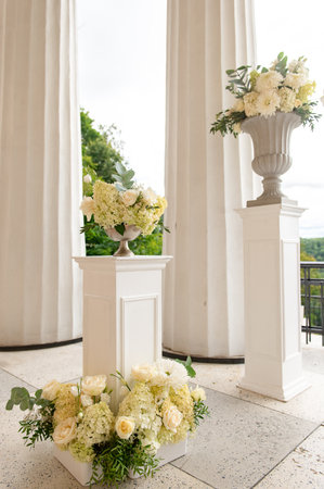 Elegant wedding floral pedestals with white roses and hydrangeas arranged on a ceremony terrace.の写真素材