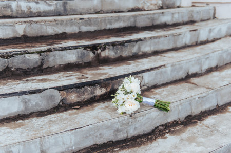 White wedding bouquet placed on worn stone stairs creating symbolic wedding scene in Latvia.の写真素材