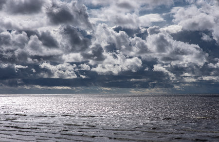 Dramatic clouded sky above the Baltic Sea in Latvia, silver reflections on water creating a peaceful...