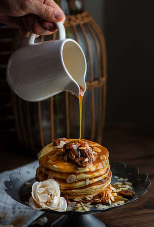 delicious pancakes with honey streaming on them from a white jug on a dark background of the kitchen...