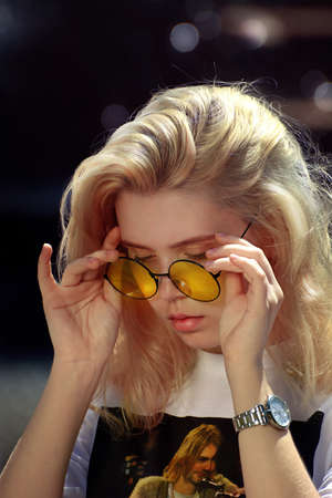 Rostov. Russia. 05/19/2019. City park. Young blonde in yellow stylish round glasses. White t-shirt with a picture of Kurt Cobain. For editorial use onlyのeditorial素材
